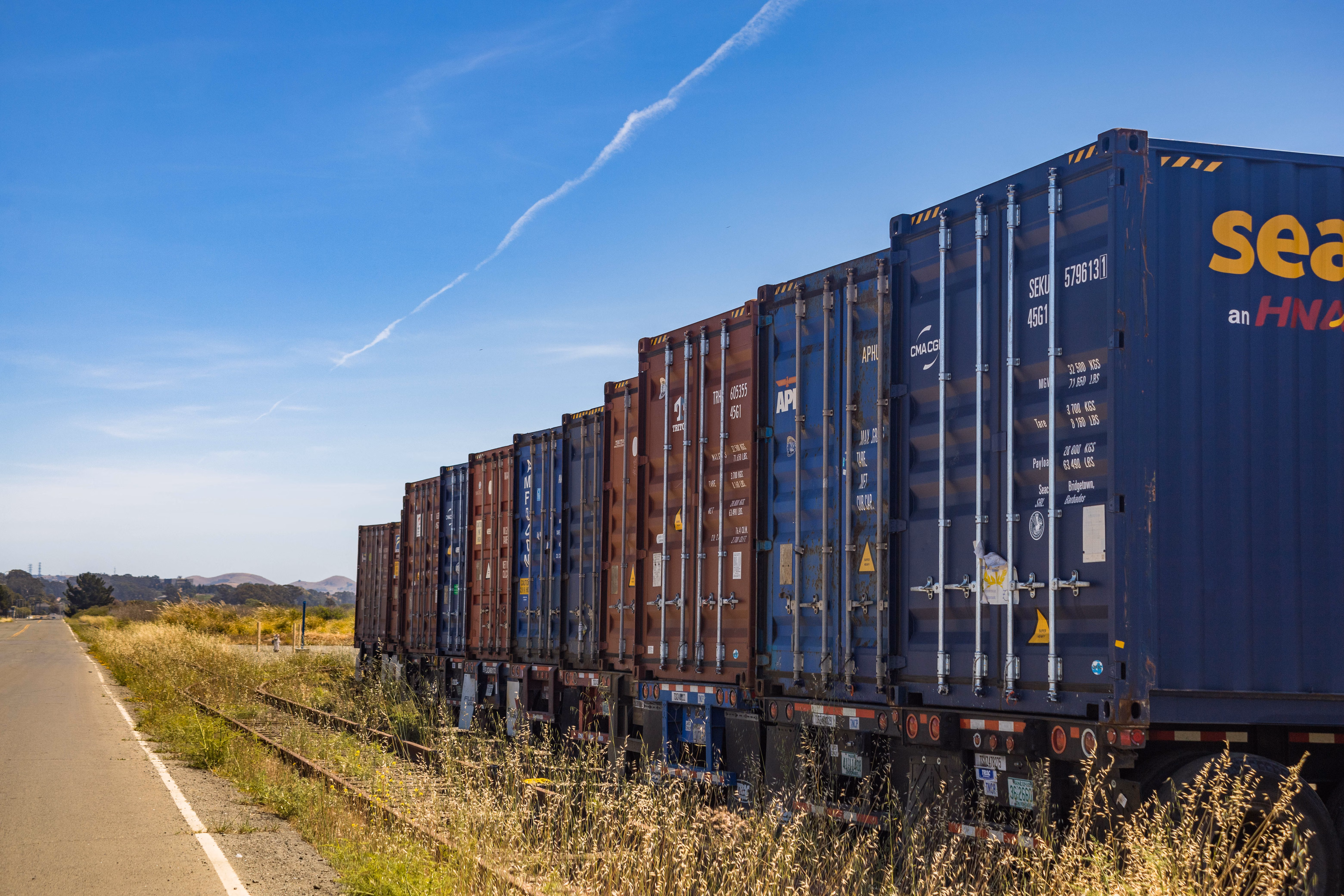 Container freight train moving along a rural railway under a clear blue sky